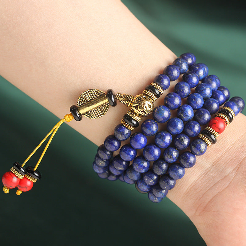 108 Lapis Lazuli mala bracelet wrapped around wrist, with brass accents and red details, symbolizing wisdom and spiritual grounding.