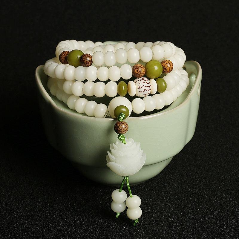 A complete view of the white jade Bodhi Mala beads with a lotus accessory, symbolizing purity and spiritual awakening, gracefully resting in a jade-green bowl.