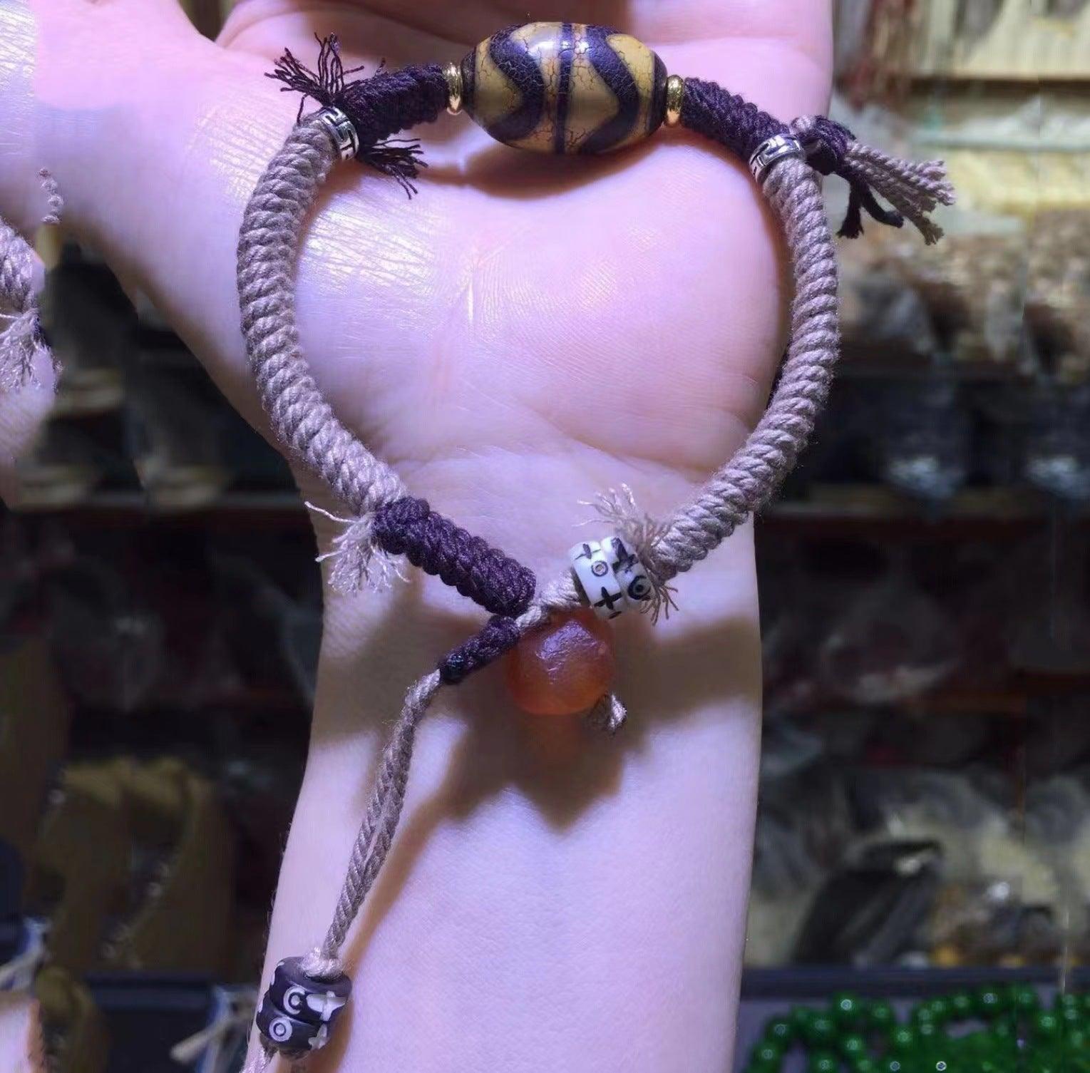 A handmade bracelet with a woven rope design, featuring a large wooden centerpiece bead and smaller decorative elements.