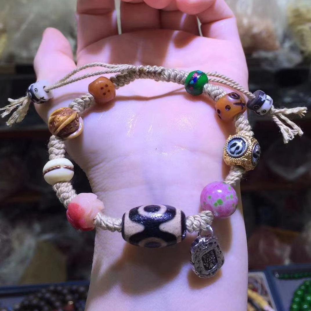 A handmade bracelet with thick rope and various colorful beads, including totem beads, pink painted beads, and a silver charm, showcasing a blend of tradition and personality.
