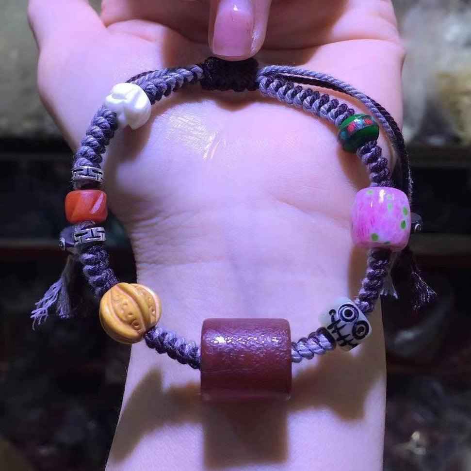 A purple braided bracelet with colorful beads, including red wood, green round, pink painted, yellow carved, and white round beads, showing unique ethnic style.