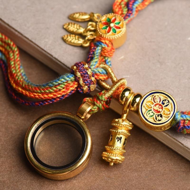 Close-up of Tibetan-style bracelet charms, featuring a prayer wheel, magnifying glass, and floral emblem, symbolizing spirituality and protection.