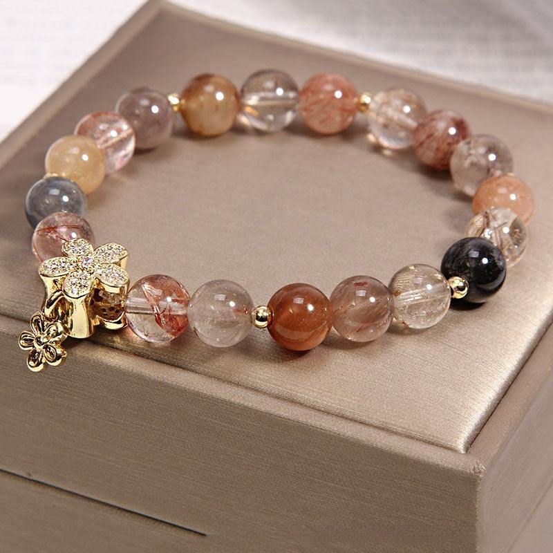 Close-up of a rutilated quartz bracelet with golden flower charm, showcasing the varied hues and textures of the beads, each with fine mineral inclusions that add depth and character.