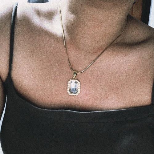 Close-up of a woman wearing a gold necklace with a rectangular crystal pendant surrounded by small diamonds, highlighting an elegant and timeless jewelry style.