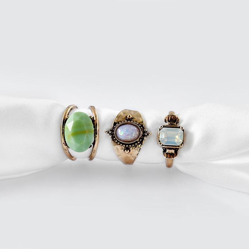 Close-up of silver rings featuring green stone, opal, and clear gemstone, emphasizing the intricate settings and vibrant colors.