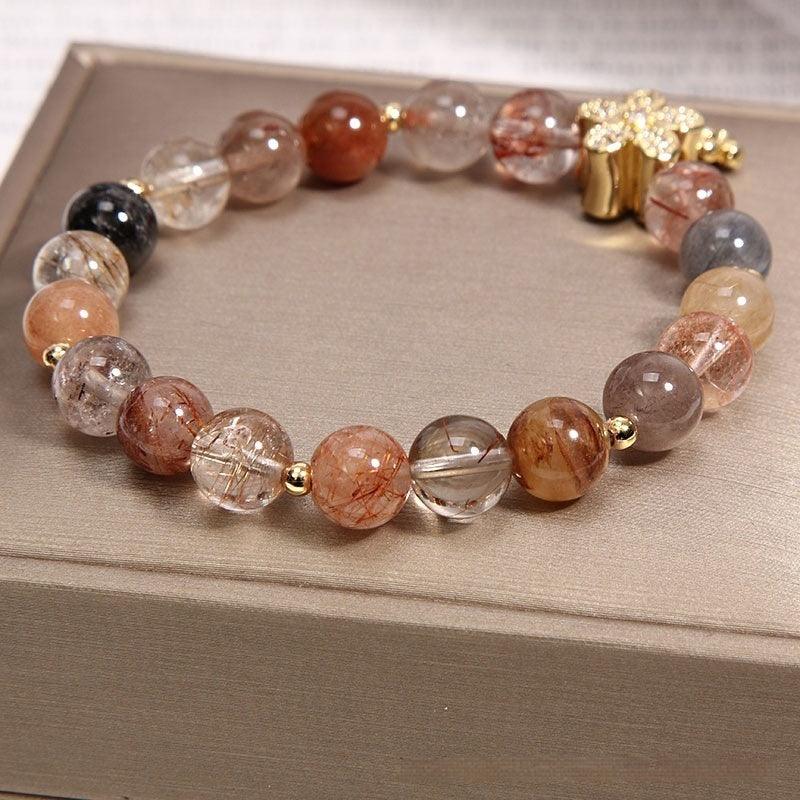 Delicate bracelet featuring round rutilated quartz beads and a sparkling gold flower charm, designed for those who seek elegance infused with natural energy.