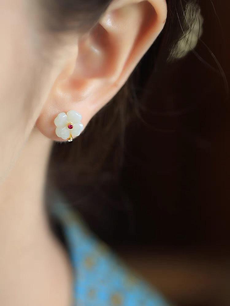 Elegant floral jade earring worn gracefully on the ear, showcasing a translucent flower design with a subtle red gemstone center, symbolizing beauty and refinement.