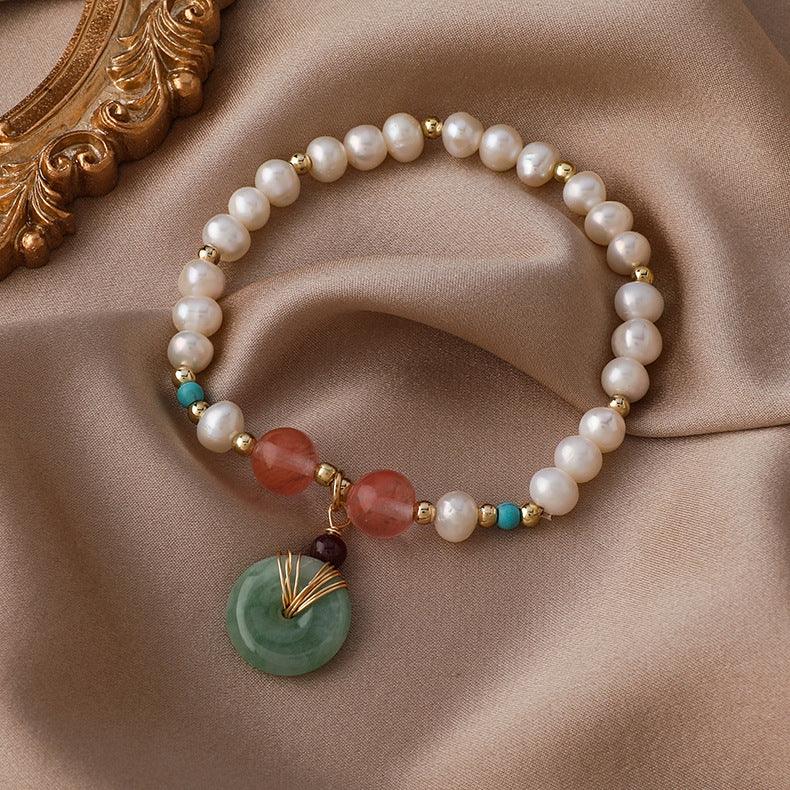 Elegant pearl bracelet adorned with red and green gemstone accents, placed on a luxurious satin background, symbolizing purity, vitality, and prosperity in various cultural beliefs.