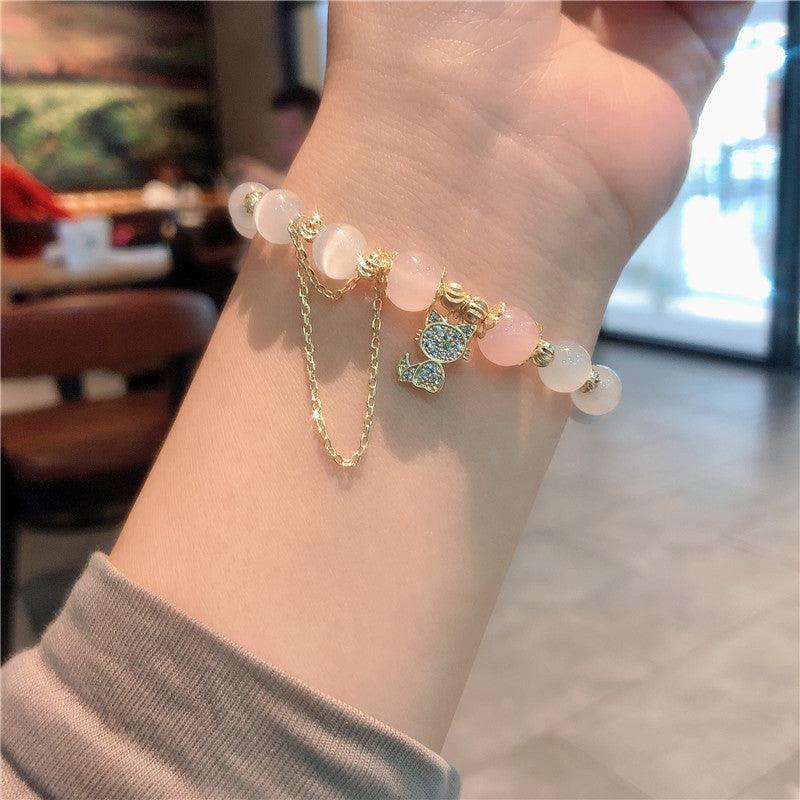 Elegant pink beaded bracelet with a sparkling gold cat charm, worn on the wrist, symbolizing love, joy, and a touch of playful luxury.