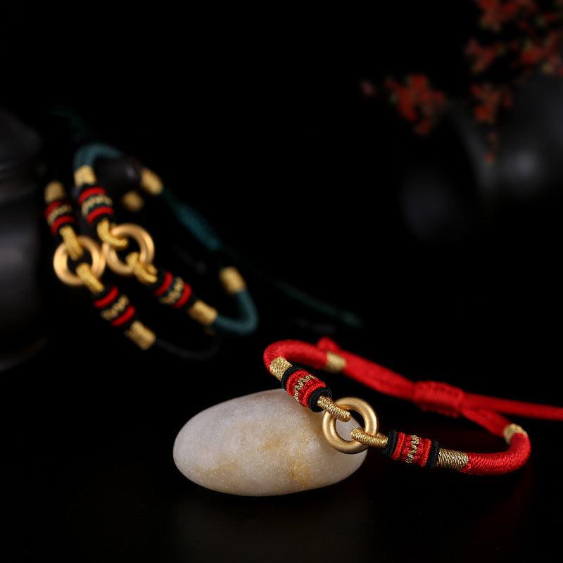 Full view of Tibetan-style bracelet with red and black woven cord, adorned with gold rings, symbolizing strength, protection, and cultural heritage.