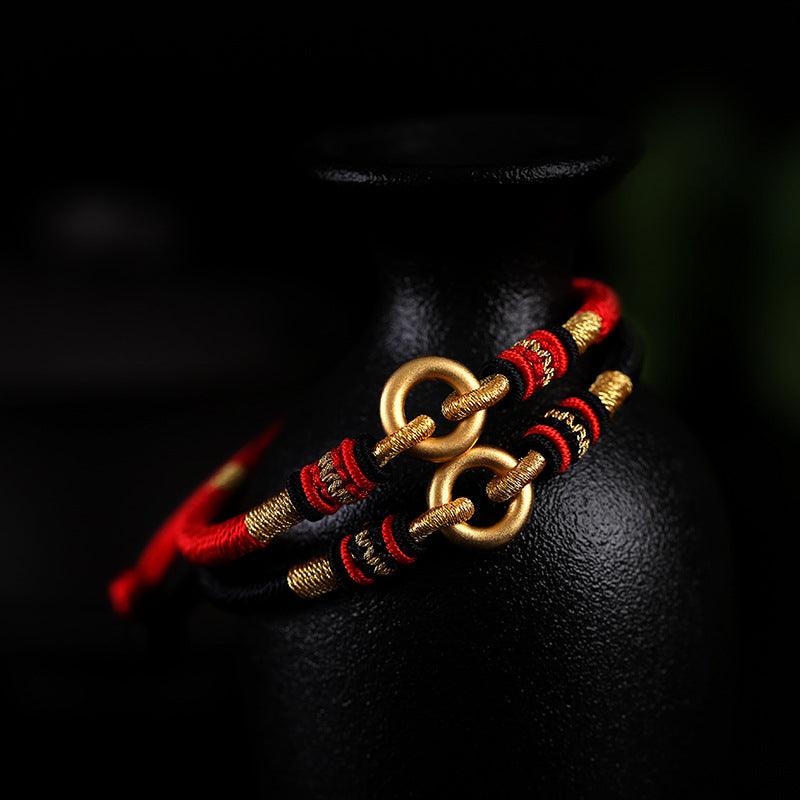 Full view of Tibetan-style bracelet with red and black woven cord and gold ring details, symbolizing cultural heritage and strength.