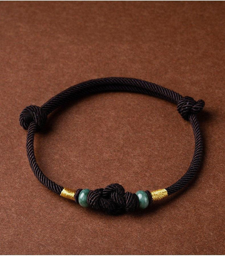 Full view of a traditional black rope bracelet with green beads and intricate knotwork, representing harmony, protection, and balance