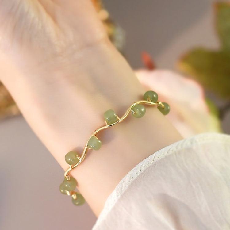 Gold bracelet with green gemstone charms, elegantly draped on the wrist.