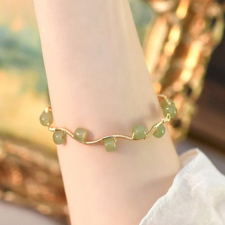 Gold wave bracelet with green gems, gracefully wrapping around the wrist.
