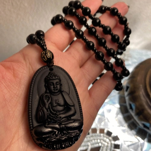 Hand holding a black Buddha pendant necklace with black prayer beads, featuring an intricately carved Buddha figure, symbolizing peace and spirituality