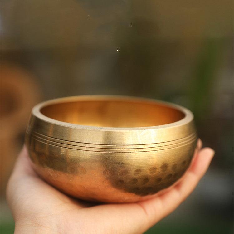 Hand holding a hammered brass singing bowl, highlighting its warm golden tones and traditional craftsmanship, often used for meditation and sound healing.