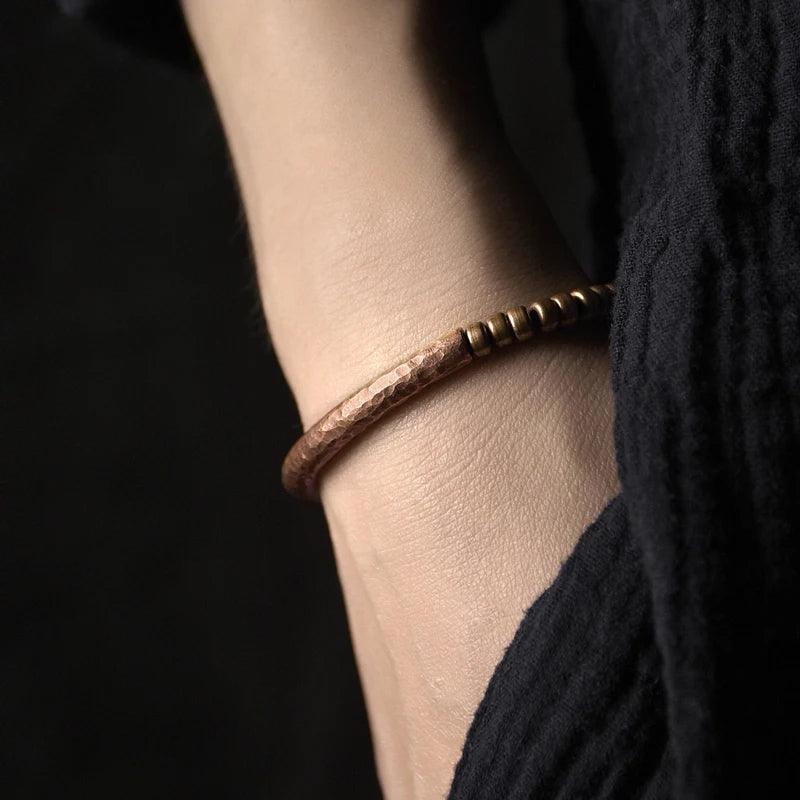 Hand wearing a hammered metal bracelet in earthy brown tones, highlighting its natural, rustic appeal and minimalist style.
