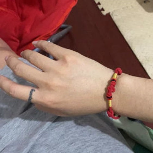 Hand wearing a red braided bracelet with yellow and black accents, showcasing a simple yet traditional style