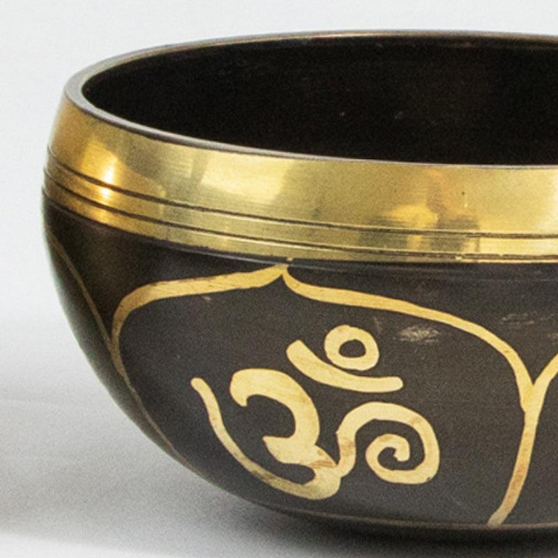 Intricately designed singing bowl with a smooth wooden mallet, resting on an embroidered cushion, highlighting traditional Tibetan craftsmanship.