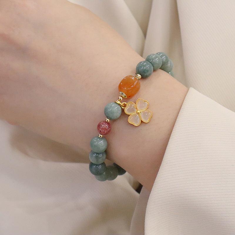 Jade beaded bracelet with red and orange accents and a four-leaf clover charm, shown elegantly on the wrist for a touch of luck and balance.