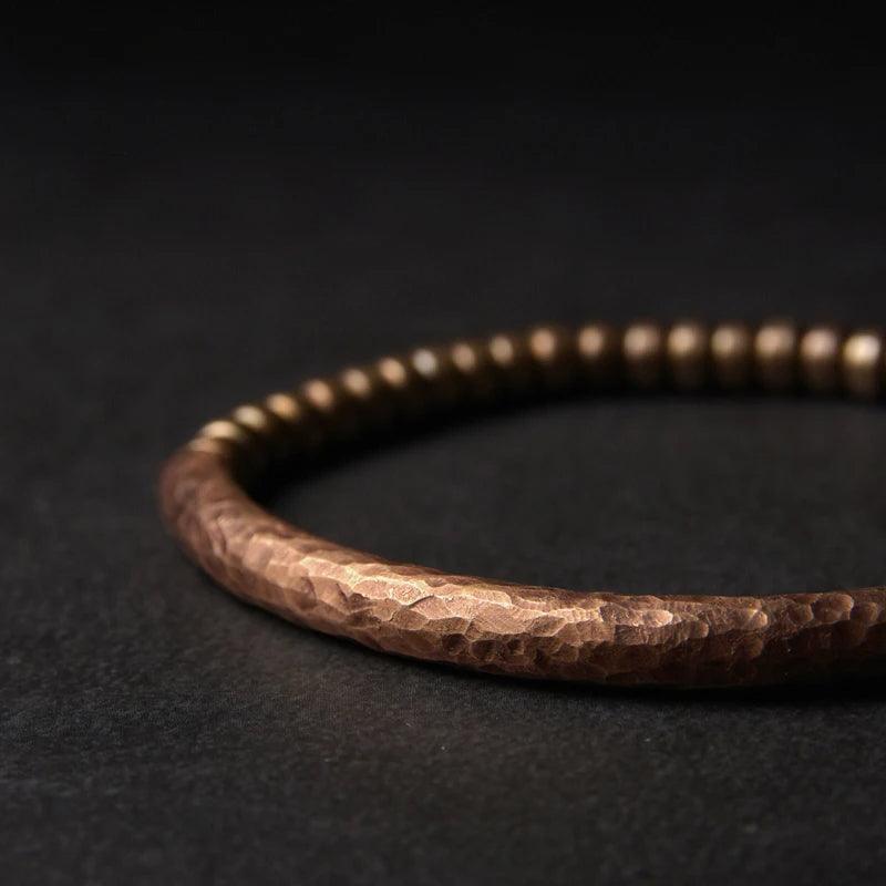 Rustic hammered copper bracelet with a minimalist design, displayed on a dark background, symbolizing strength and resilience rooted in ancient traditions.