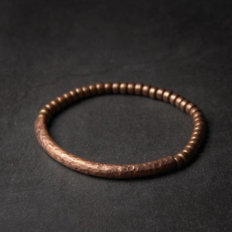 Rustic hammered metal bracelet in dark brown tones, displayed on a dark background to highlight its rugged, handcrafted design.
