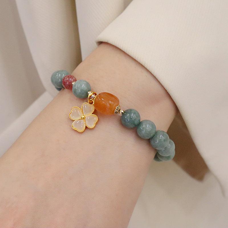 Stylish jade beaded bracelet with red and orange stones and a four-leaf clover charm, elegantly displayed on the wrist.
